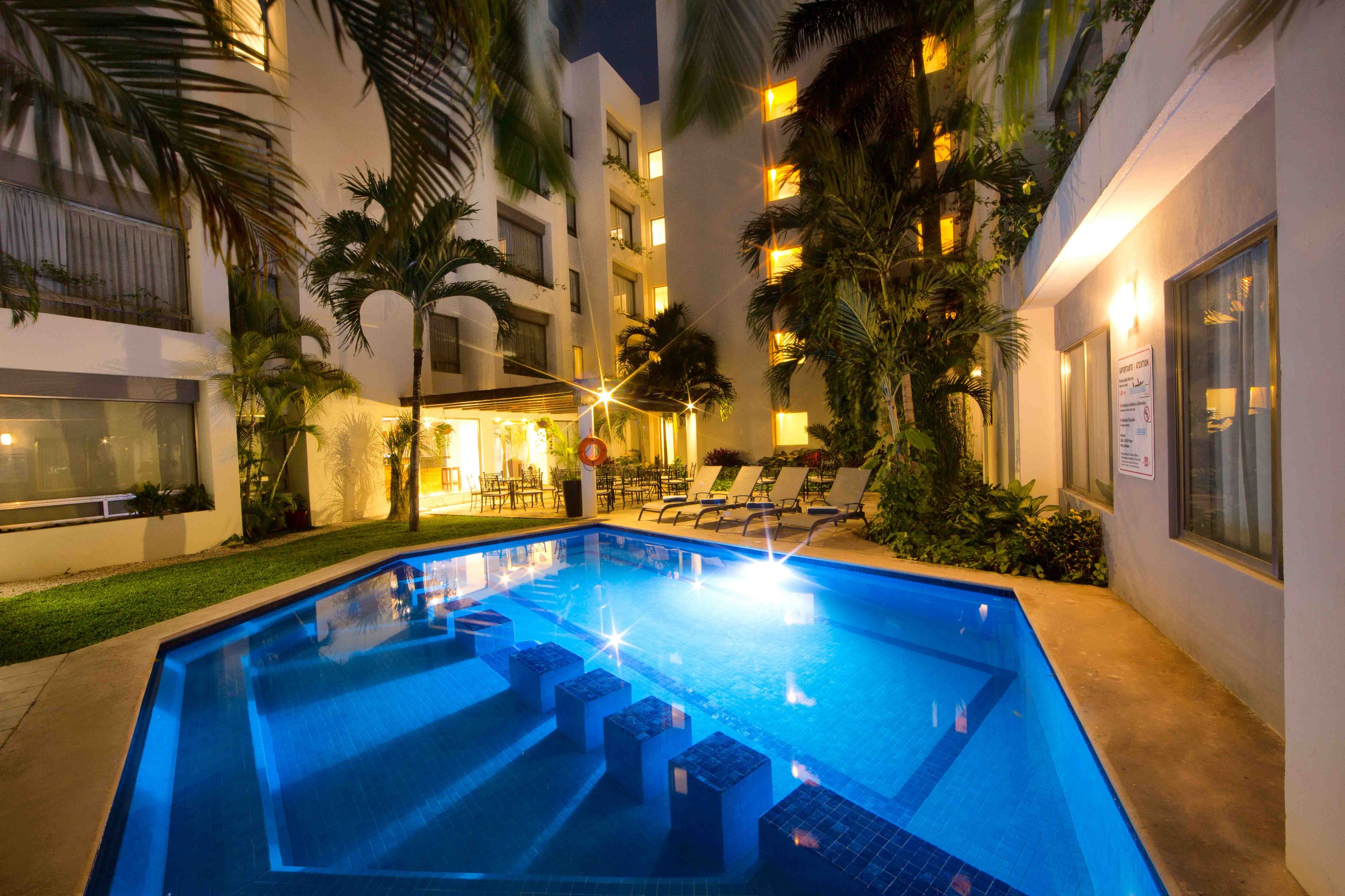 Illuminated pool at night surrounded by palm trees at Ambiance Suites