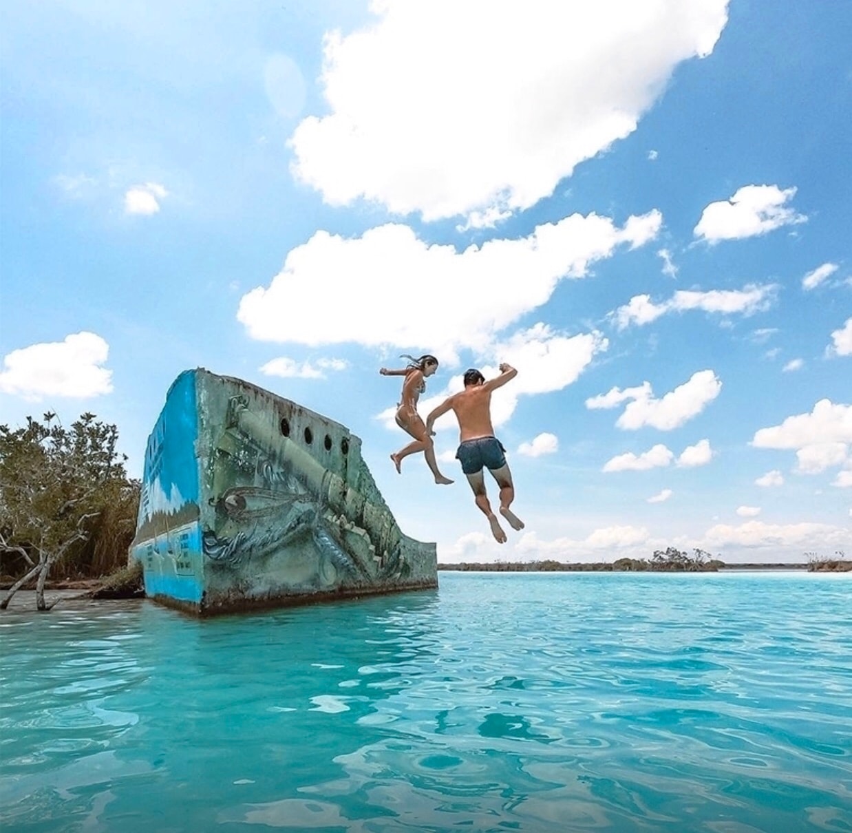 Couple jumping off the iconic painted shipwreck into Bacalar Lagoon