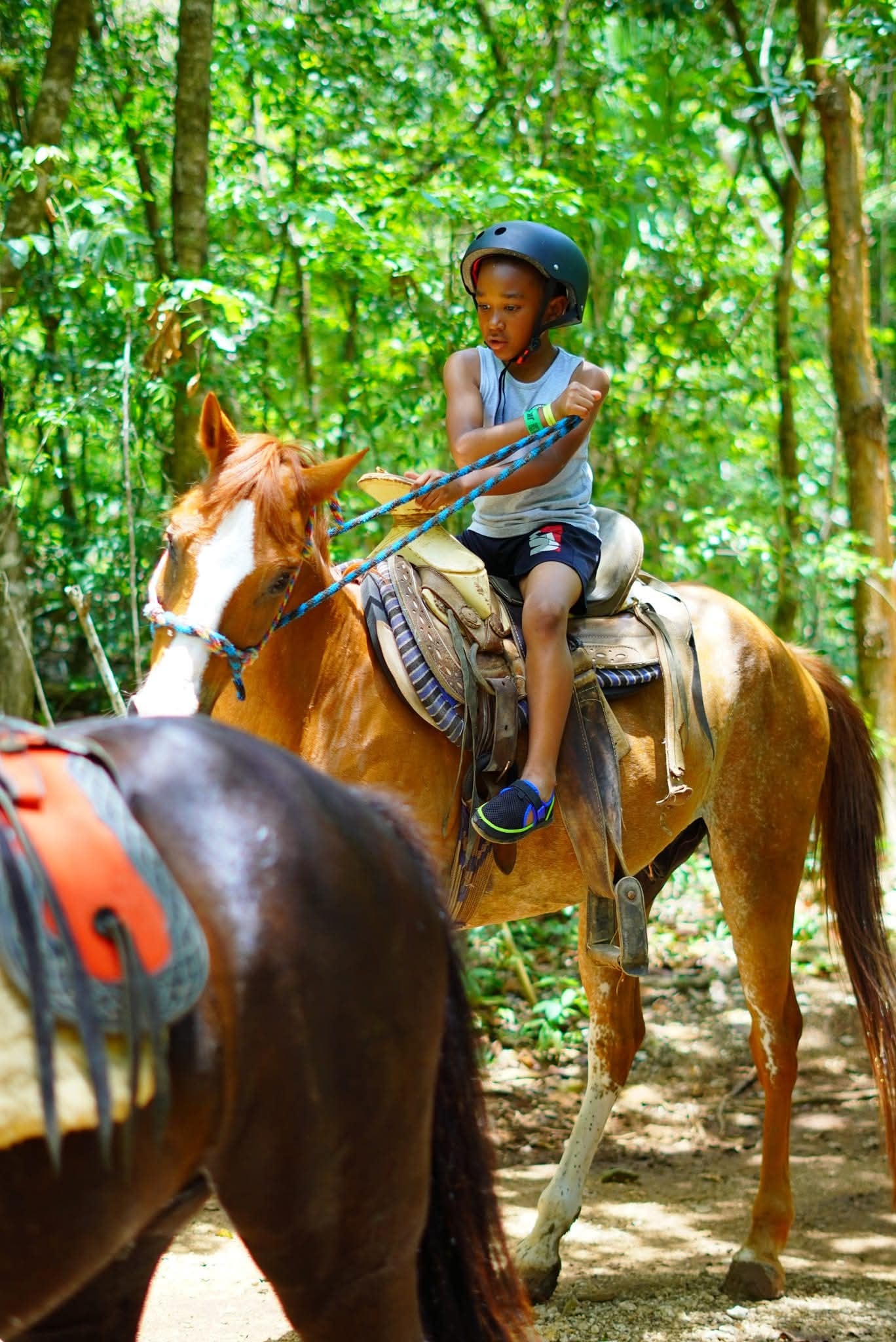 Young boy with helmet riding a horse through the Cancun jungle