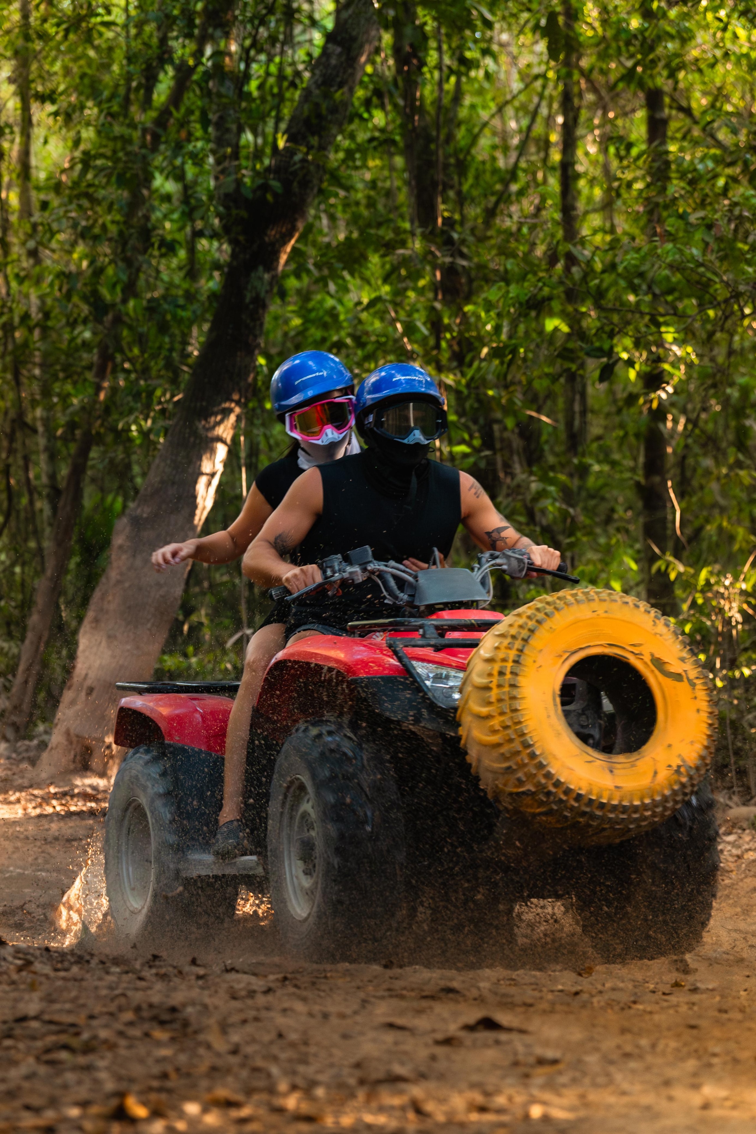 Couple riding a red ATV through the jungle, kicking up mud and dust