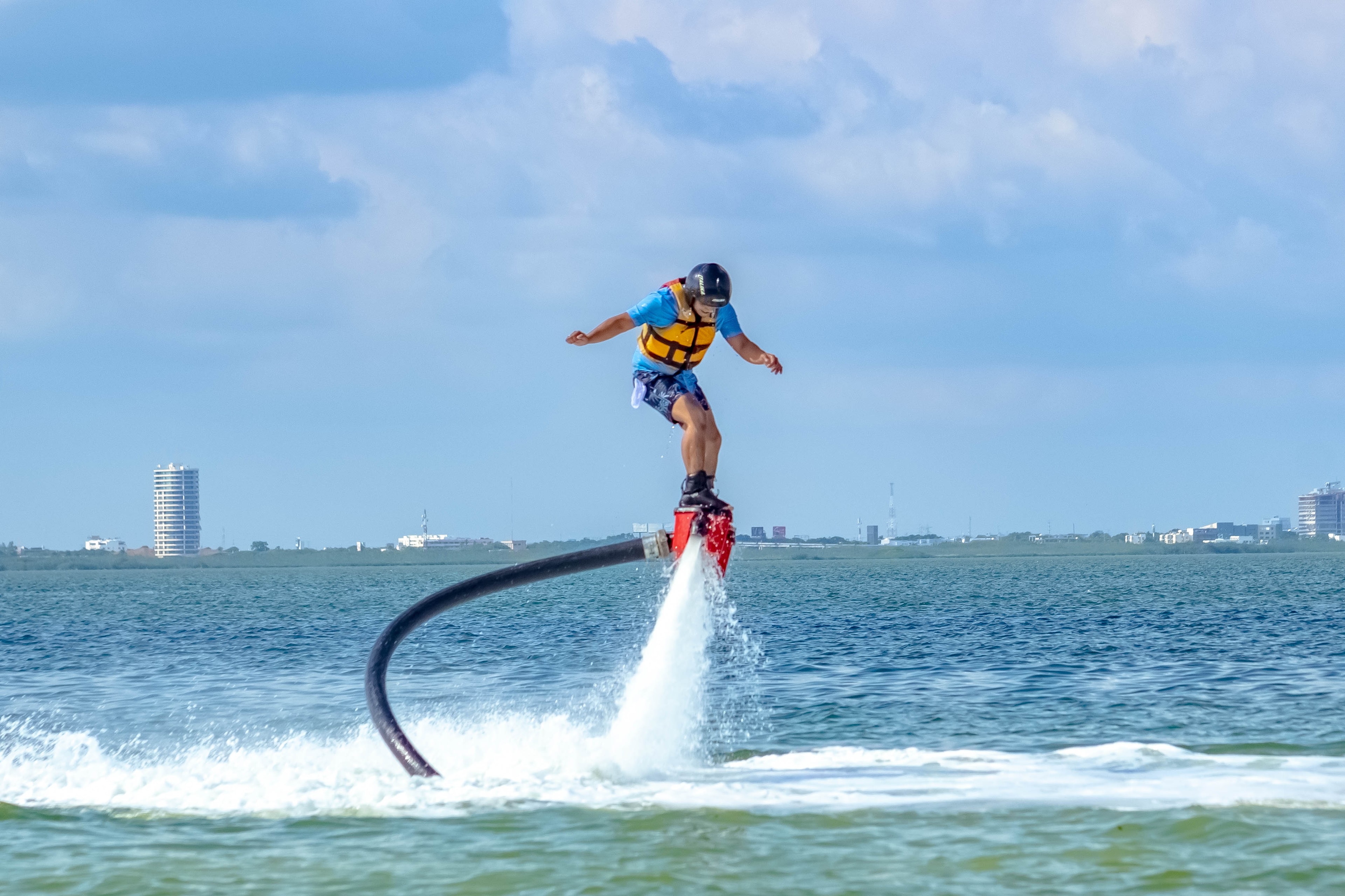 Man standing upright on a flyboard hovering above the Cancun lagoon with the city skyline behind