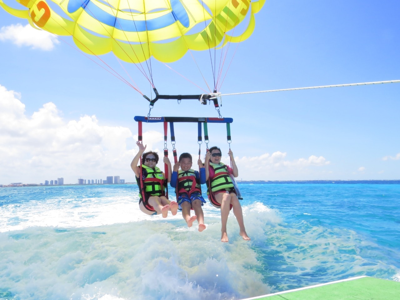 Family of three lifting off the water on a parasail with the Cancun Hotel Zone in the background
