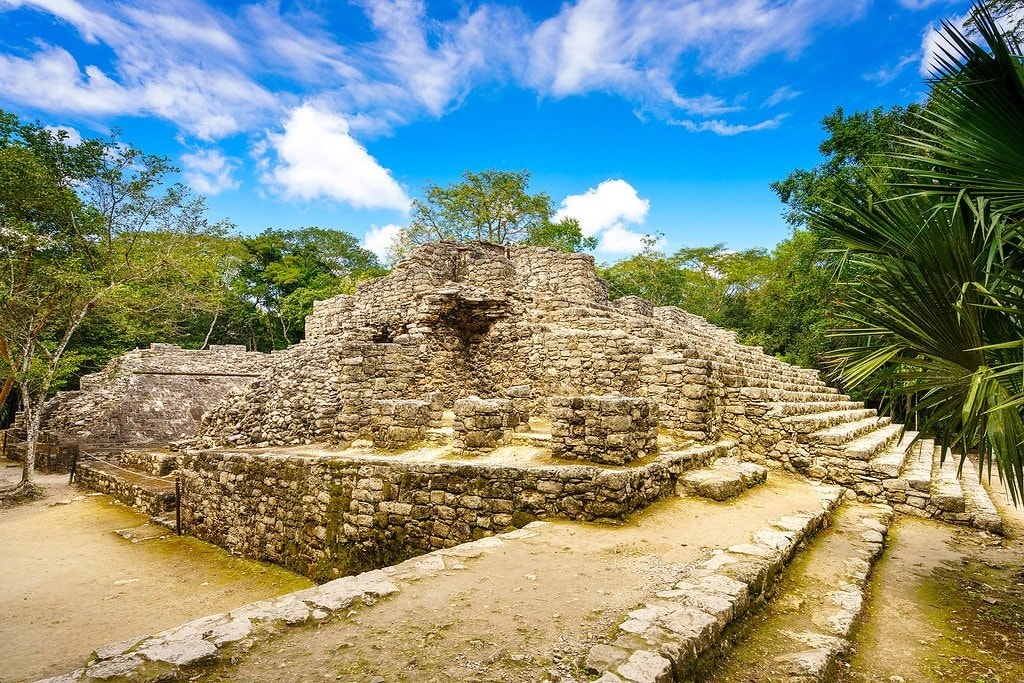 Cobá ball court ruins surrounded by tropical jungle and blue sky