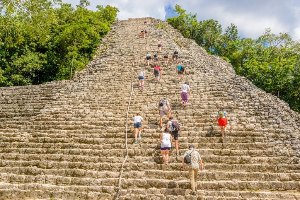 Tourists climbing the steep stone steps of the Nohoch Mul pyramid at Cobá